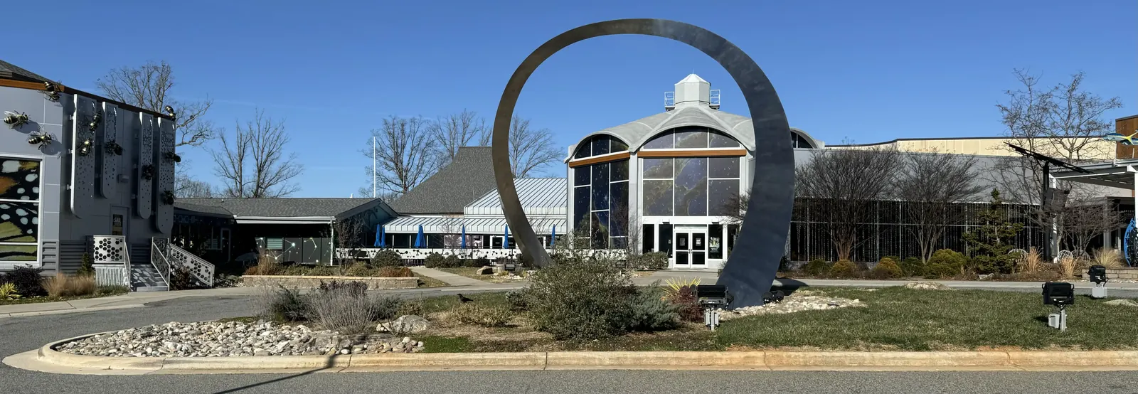 Front view of Greensboro Science Center with a large metallic Archway and butterfly wing design on the adjacent building.