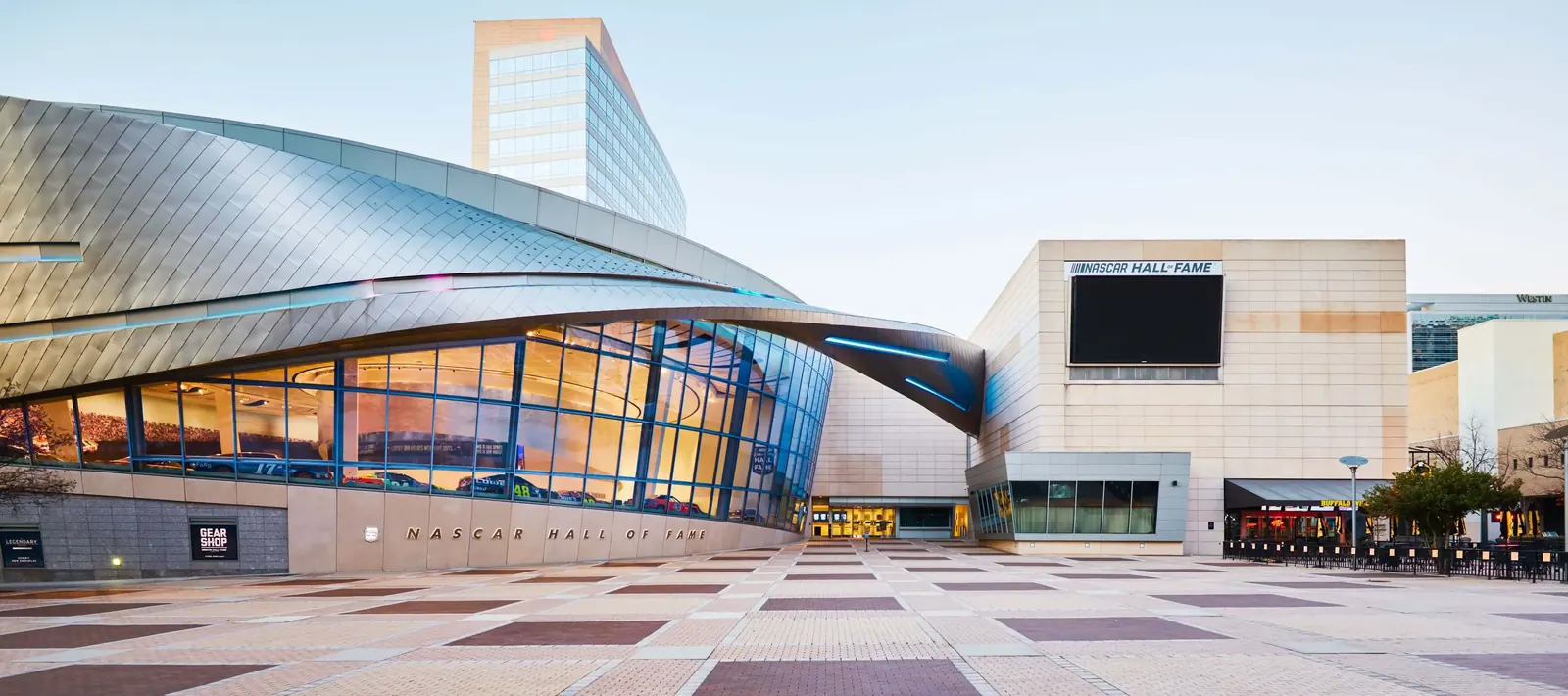 Modern NASCAR Hall of Fame building with curved architecture and glass facade illuminated by soft sunlight.