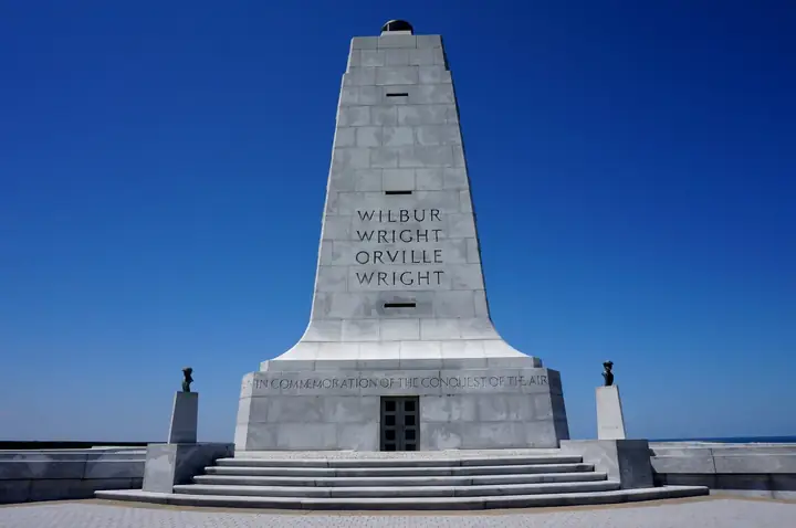 Wright Brothers National Memorial monument with names Wilbur and Orville engraved, under blue sky.
