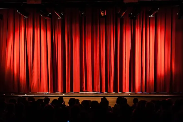 Closed red curtains on the stage at Raleigh Little Theatre with audience in foreground.