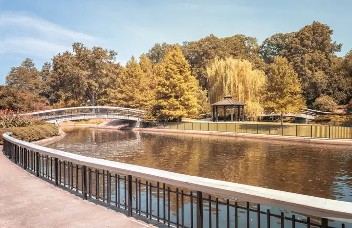 Serenely lit Pullen Park featuring a calm lake, a footbridge, and gazebo amid vibrant autumn foliage.