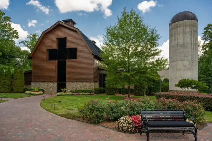 Exterior view of the Billy Graham Library with a barn-like structure, brick pathway, blooming rose bushes, and a silo.