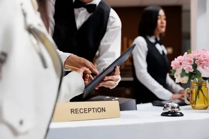 Welcoming reception desk at Hatteras Island Inn with staff assisting a guest, bell, and flower arrangement visible.
