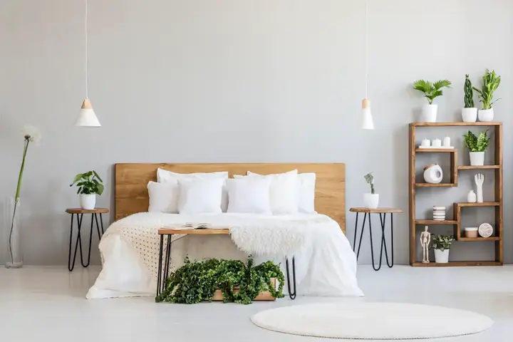 Elegant and serene bedroom at Oasis Suites Hotel with white bedding, wooden headboard, hanging lights, and decorative plants.