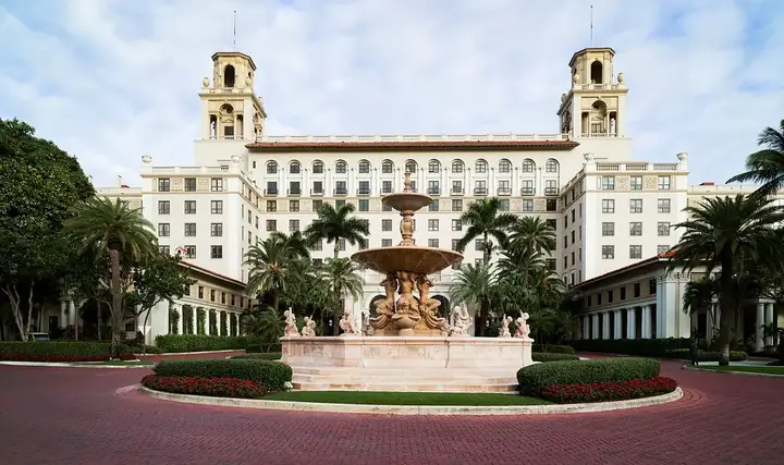 The Breakers Resort facade with ornate fountain, manicured gardens, and towering palm trees.