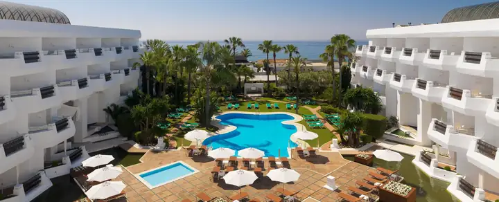 Aerial view of Coral Beach Resort & Suites showcasing the large blue swimming pool, surrounding sun loungers, palm trees, and adjacent beach.