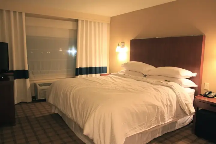 Alt text: "Well-appointed guest room at Four Points by Sheraton Raleigh Arena with a cozy queen bed, crisp white linens, and warm ambient lighting."