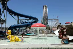 Visitors enjoy various water attractions at Myrtle Waves Water Park with slides, fountains, and a giant yellow duck structure.