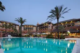 Twilight view of Hilton Myrtle Beach Resort featuring an illuminated pool area with palm trees and hotel facade.