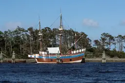 Historical replica ship docked at Roanoke Island Festival Park, surrounded by water and forest.