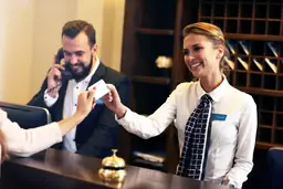 Front desk at Outer Banks Inn with smiling staff assisting guests, handing over a key card.