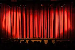 Closed red curtains on the stage at Raleigh Little Theatre with audience in foreground.