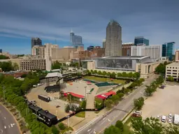 Aerial view of Red Hat Amphitheater with stage and seating area, surrounded by Raleigh cityscape under a clear sky.