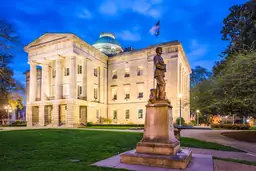 Twilight view of the State Capitol building with a statue in the foreground and American flag flying at half-mast.