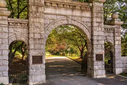 Arched stone entrance of Historic Oakwood Cemetery with wrought iron gates and surrounding greenery.