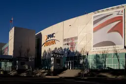Exterior view of PNC Arena with parking lot, colorful trees, and flags under a partly cloudy sky.