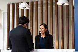 Hotel reception scene with a smiling female employee assisting a male guest at Canopy by Hilton Raleigh North Hills.