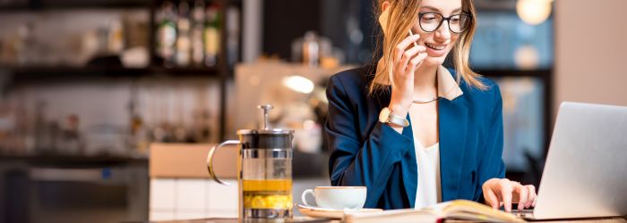 Woman in a coffee shop working on her laptop and talking on the phone