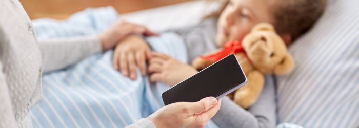 A mother in bed with her sick kid sending a message to school requesting absence