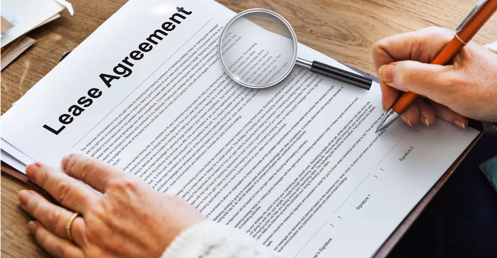 A person using magnifying glass to view a lease agreement whilst signing it. 