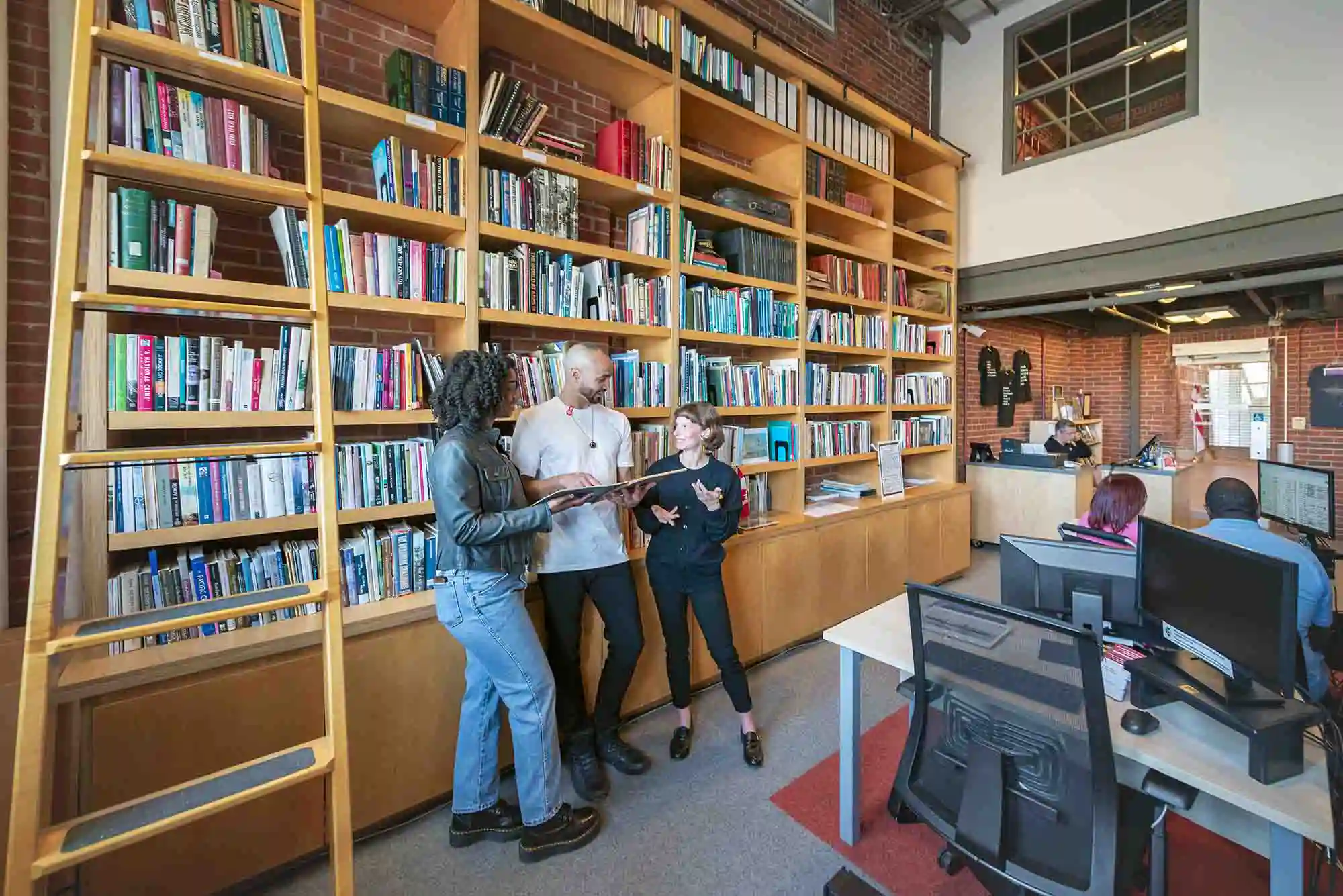 A couple speak to a representative from Pier 21 while standing against a wall of books.