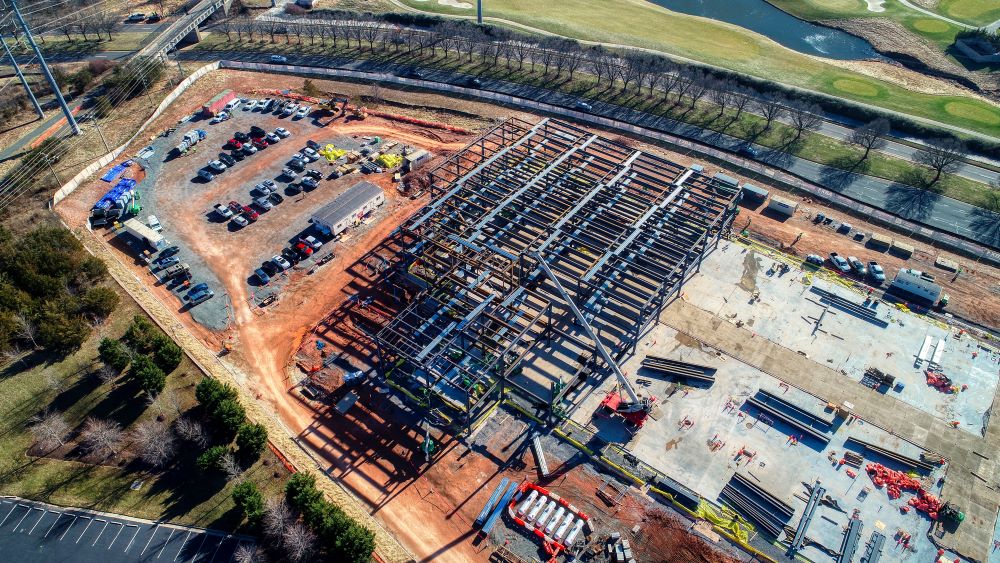 A drone view of a data center, featuring large buildings and a parking lot surrounded by greenery.