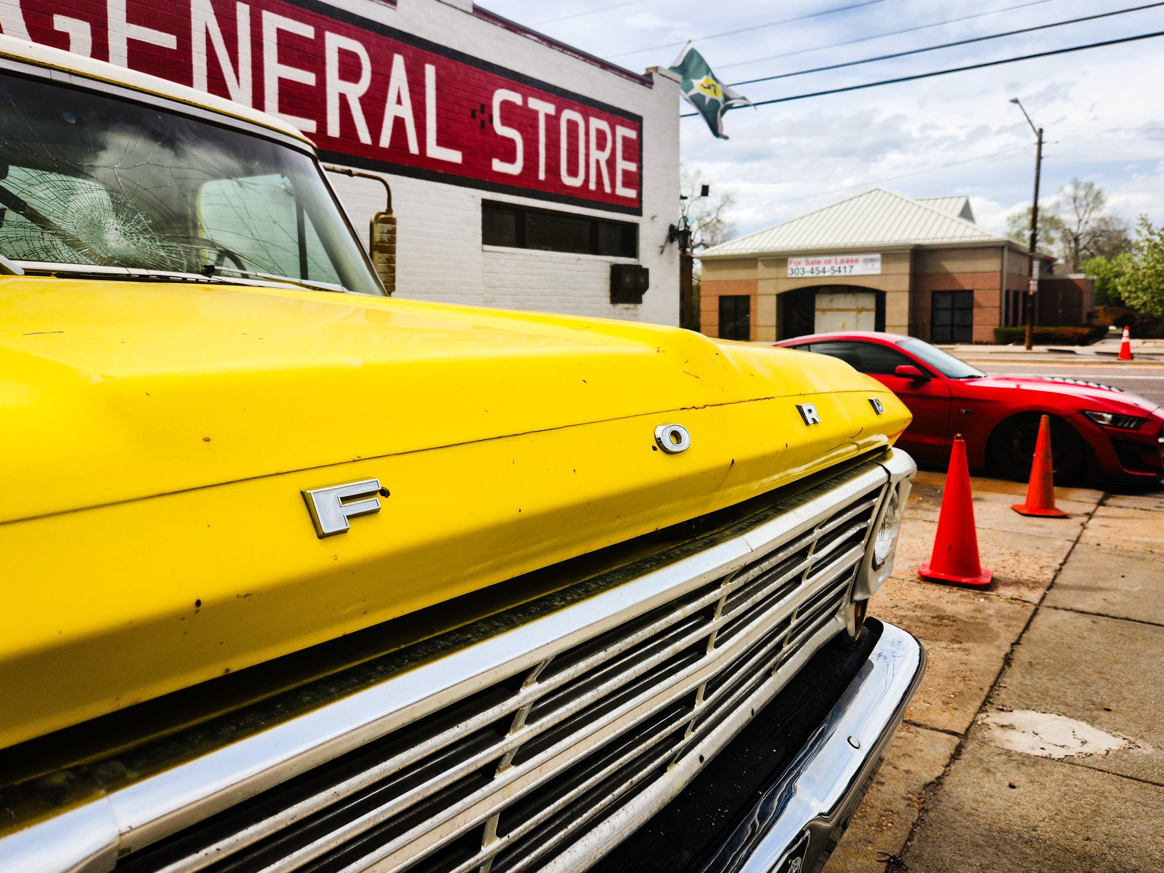 An older, 1950's Ford pickup truck in the foreground with a Ford Mustang GT500 in the Background parked by a general store in colorado