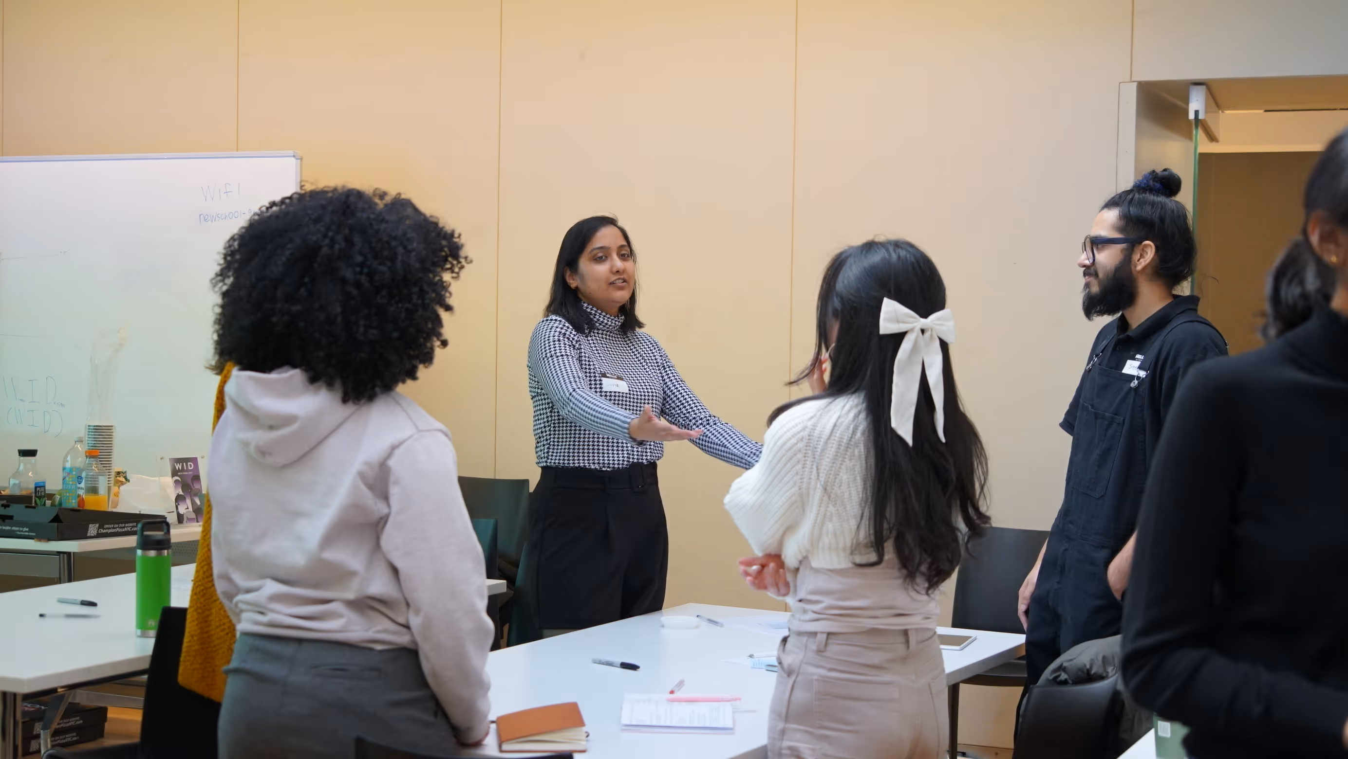 A woman speaking and gesturing with her hands to a group of four people gathered around a table in a meeting room.