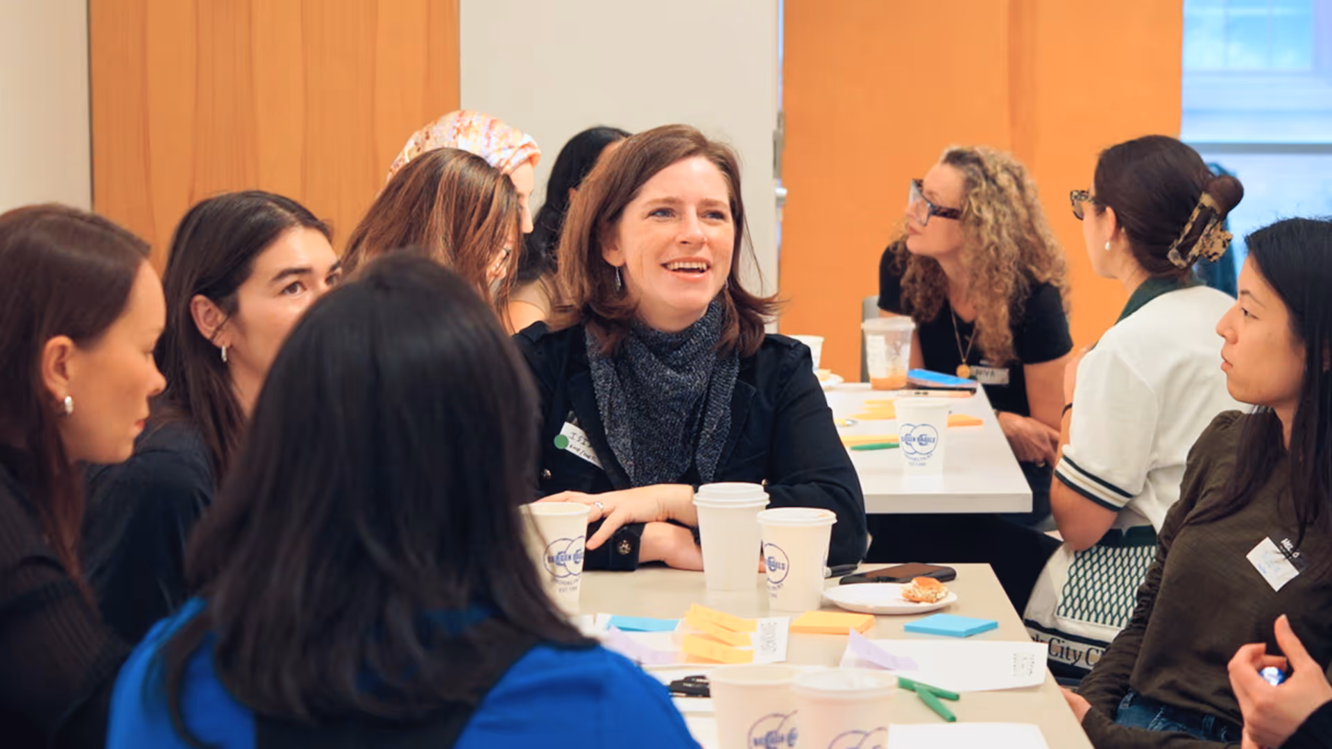 Group of diverse women engaged in a discussion around a table with coffee cups and sticky notes.