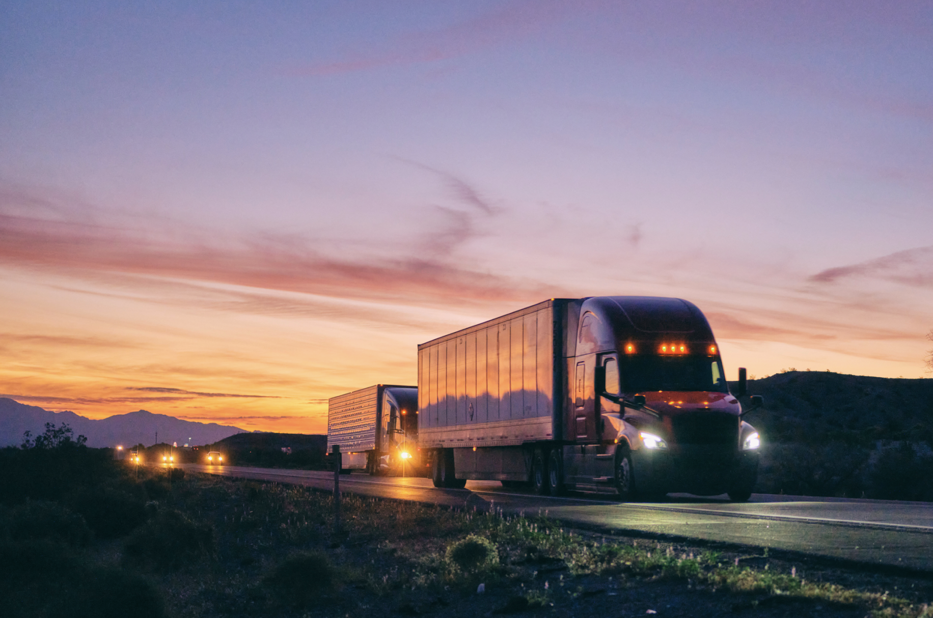 Two semi trucks hauling shared truckload trailers on a highway at sunset