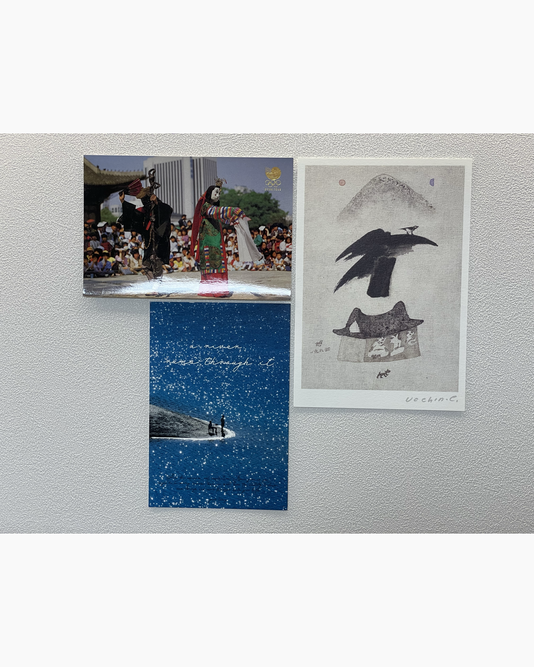 세 장의 그림이 흰 벽에 붙어 있음. 왼쪽 위는 전통 탈춤 공연 사진, 오른쪽은 새와 집이 있는 동양 수묵화 스타일의 그림, 아래쪽은 별이 반짝이는 파란 하늘 아래 강가에 앉아 있는 사람 두 명의 사진이 담긴 엽서.