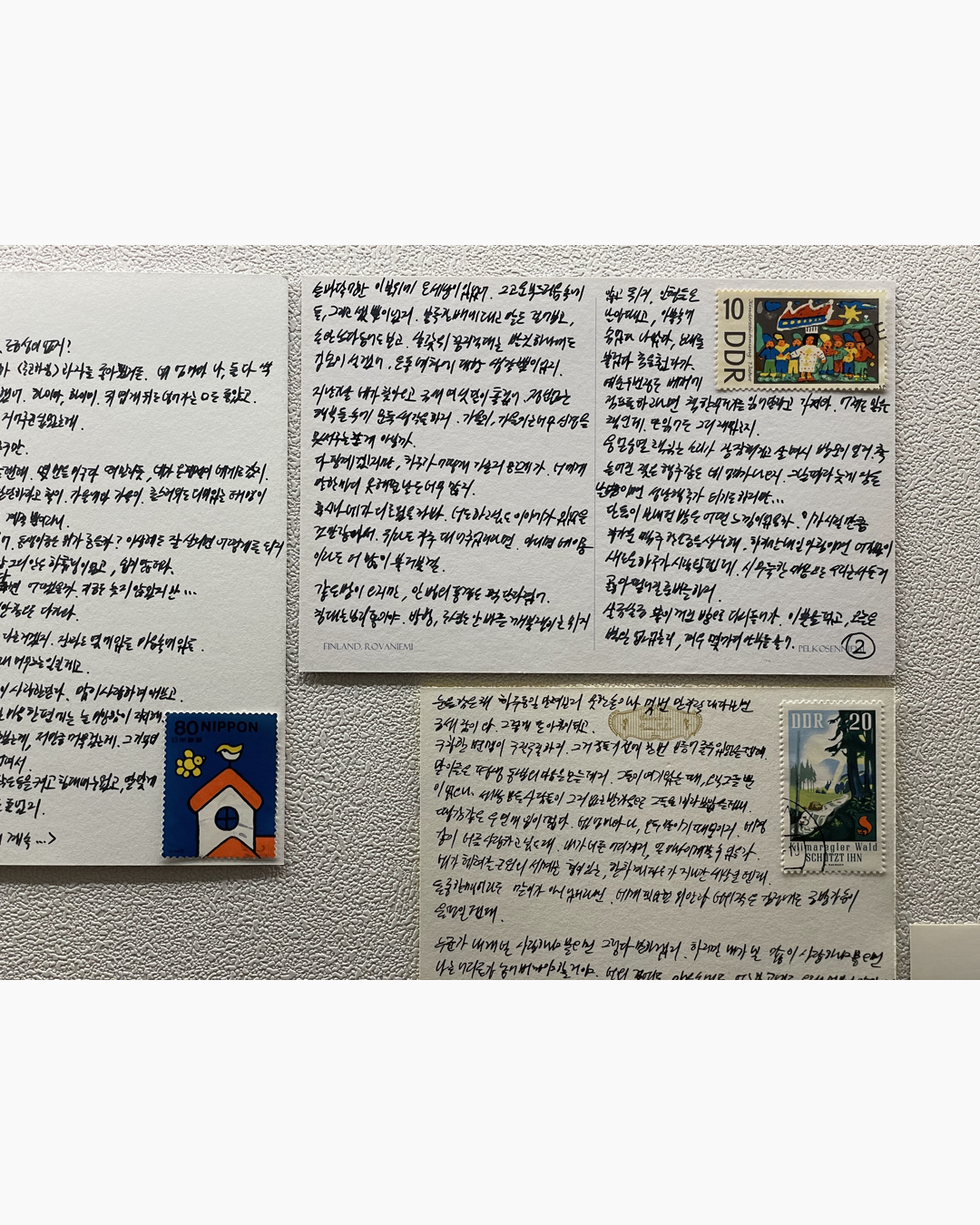 손글씨로 된 세 장의 엽서가 벽에 붙어 있고, 각 엽서에는 일본과 동독의 우표가 붙어 있다.