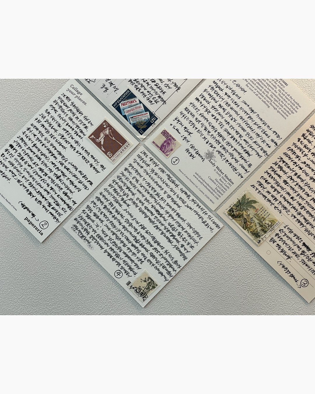 네 장의 한글 손글씨가 적힌 엽서가 테이블 위에 놓여 있고 각 엽서에는 다양한 우표가 붙어 있다.