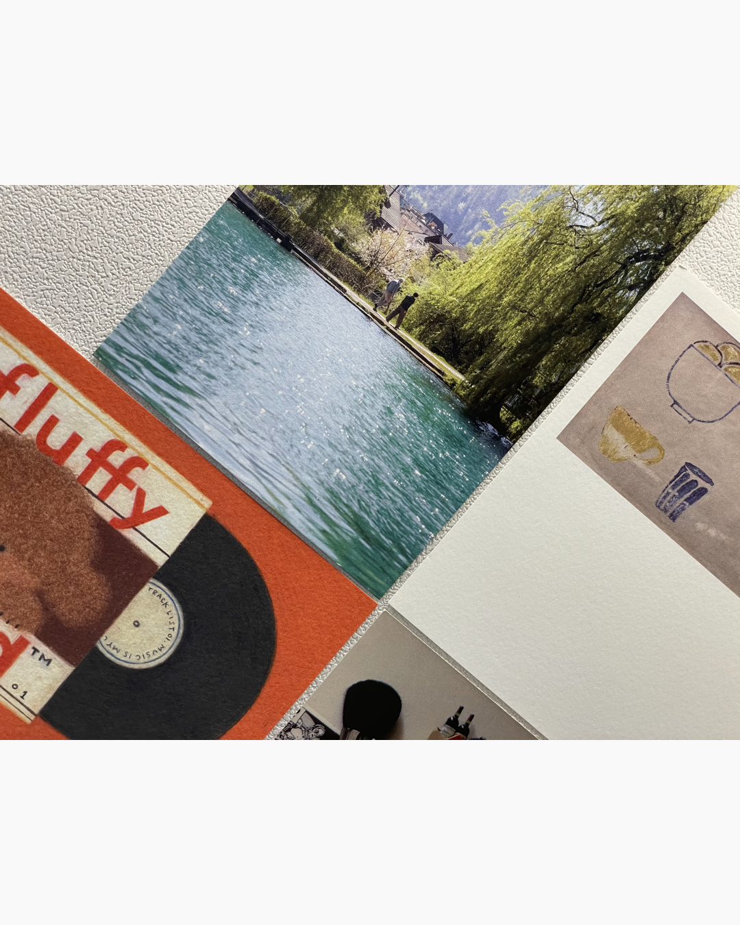 호수 옆 산책로를 걷는 두 사람이 있고, 주변에 녹색 나무들과 건물이 보이는 풍경 사진과 주황색 배경에 곰 인형과 검은색 레코드판이 있는 이미지, 그리고 컵과 그릇이 스케치된 그림이 나란히 붙어 있는 모습.