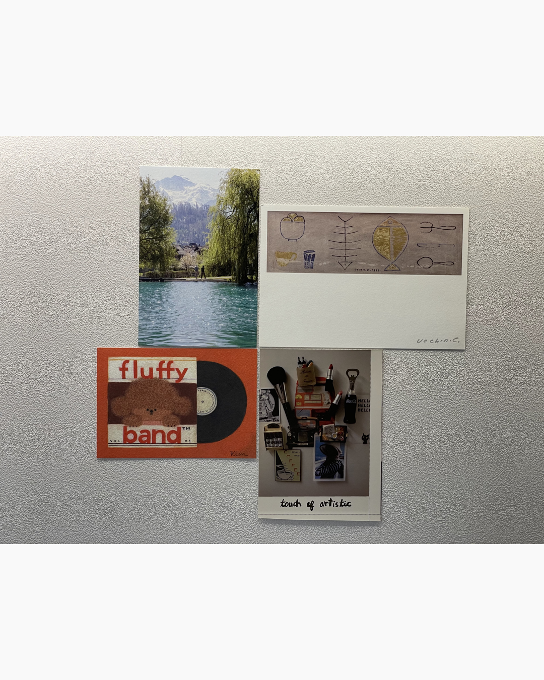 벽에 자석으로 붙여진 풍경 사진, 낙서가 그려진 엽서, 'fluffy band' 레코드 그림, 그리고 예술적인 도구 사진이 모여 있음.