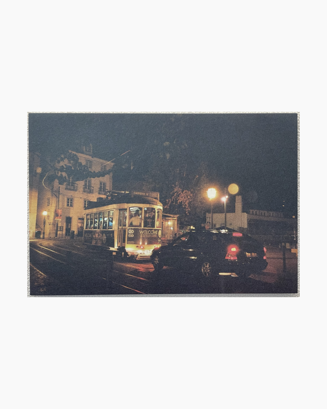 밤에 불이 켜진 트램과 검은색 자동차가 도시 거리에서 정차해 있다.