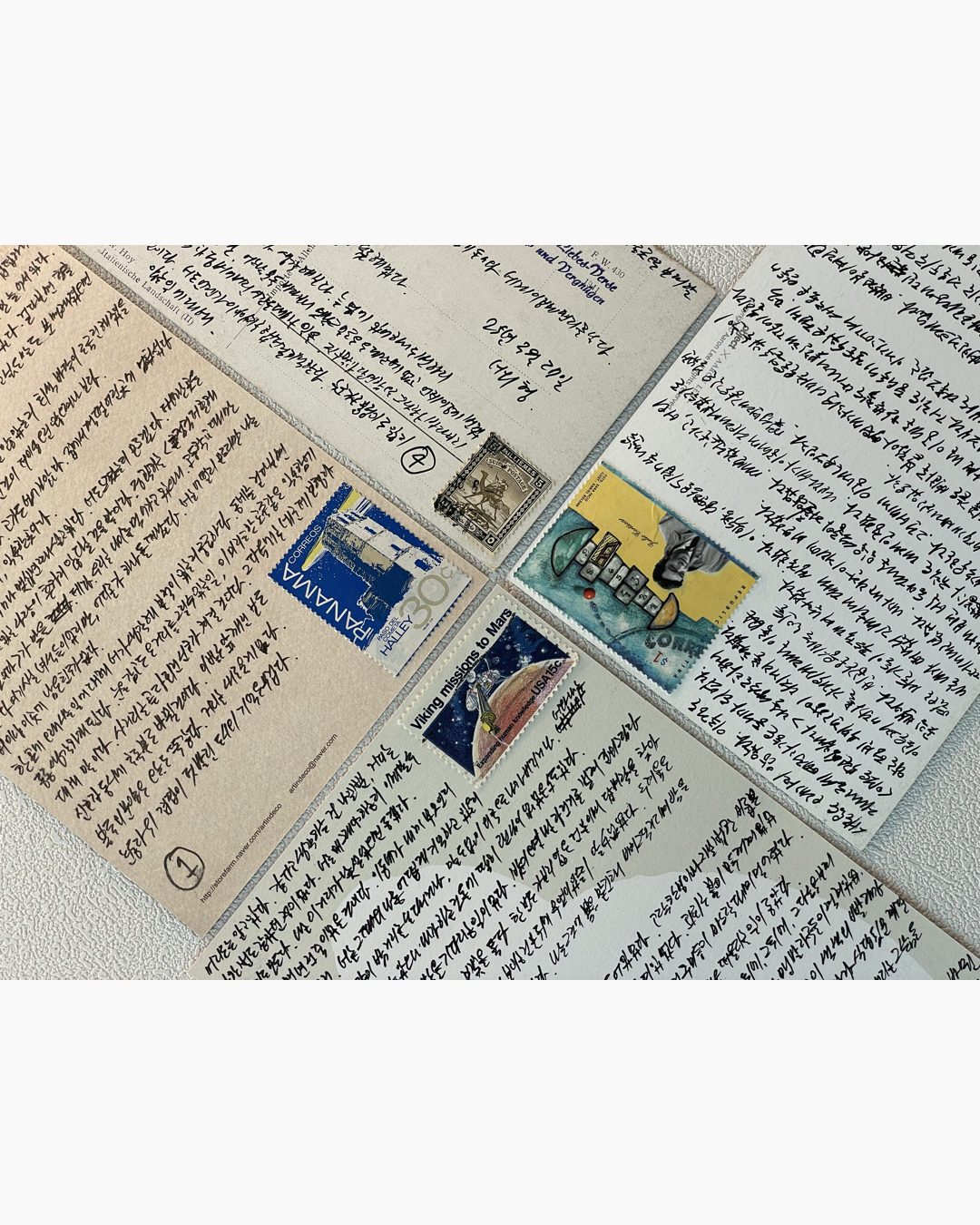 여러 개의 한국어로 손글씨가 적힌 엽서들이 겹쳐진 모습과 우표들.