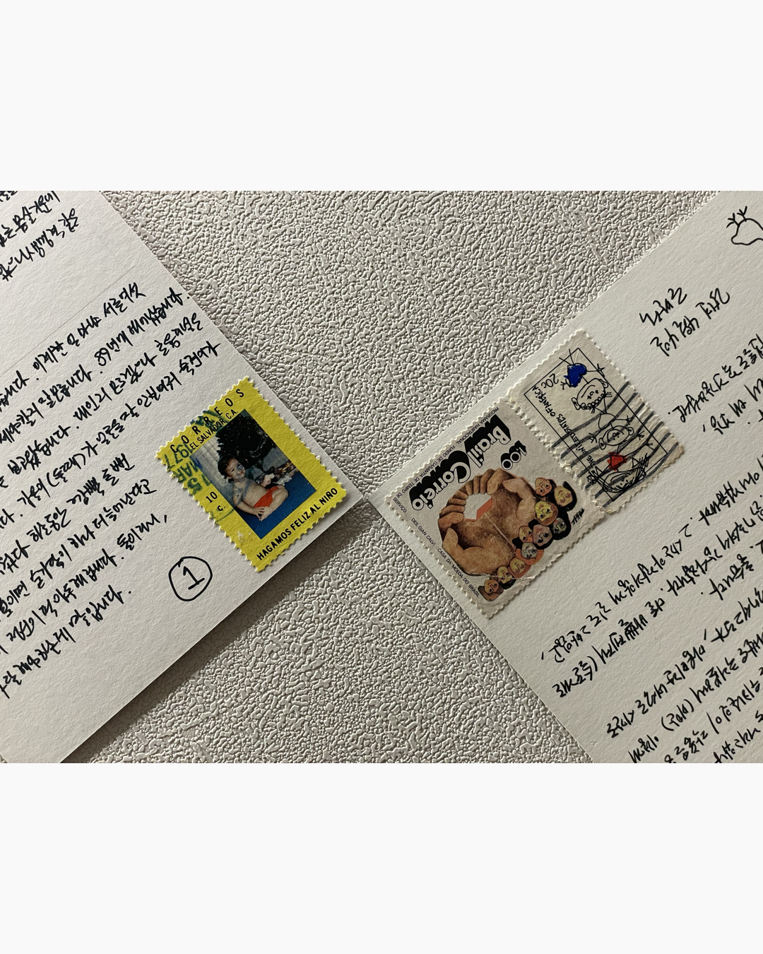 두 개의 손글씨 편지 모서리에 각각 다양한 우표가 붙어 있다. 왼쪽 편지에는 노란색 테두리의 아이 사진 우표가, 오른쪽 편지에는 여러 인물 그림과 만화 스타일의 작은 도장이 있는 우표가 붙어 있다.