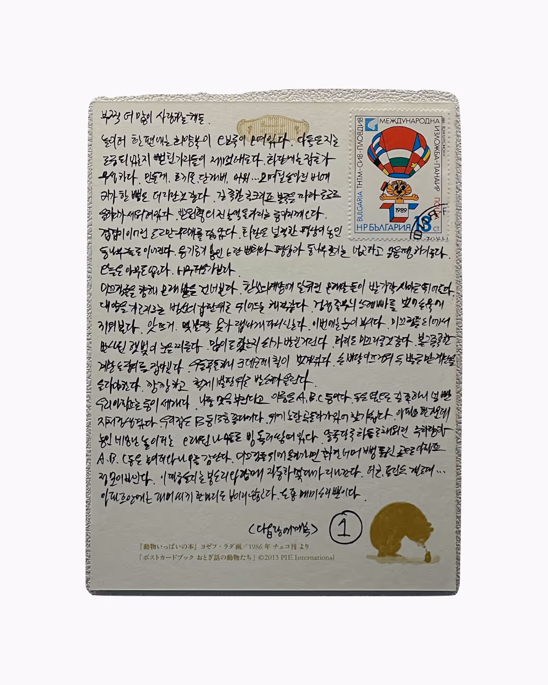 다양한 문자가 빽빽하게 적힌 엽서 뒷면과 1989년 국제 우표, 하늘색과 빨강색 열기구 그림이 있는 우표가 부착되어 있음.