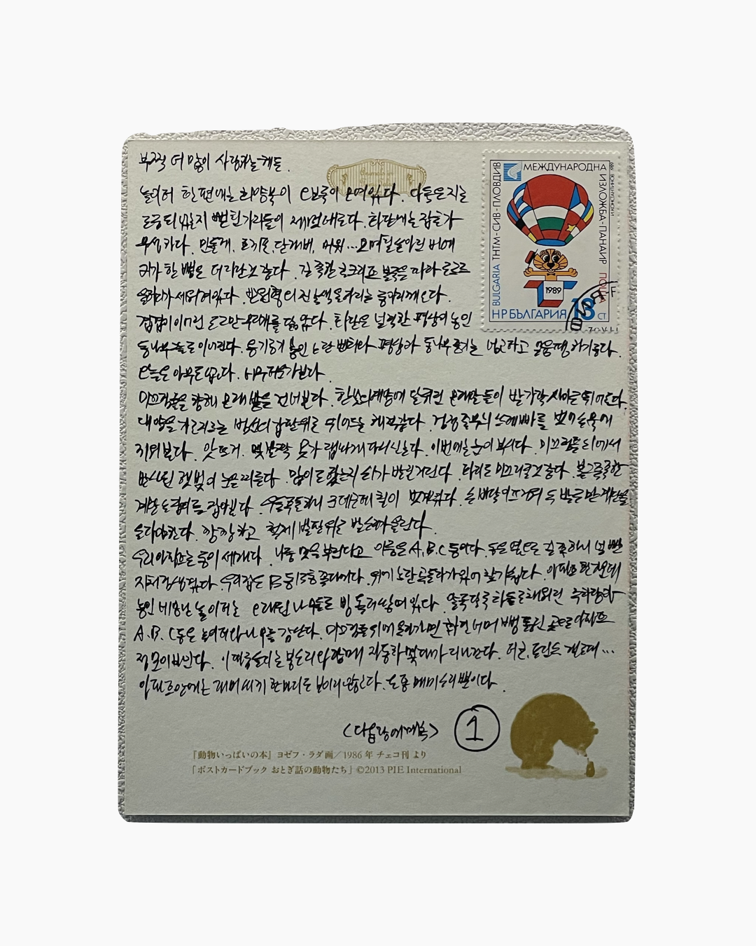 다양한 문자가 빽빽하게 적힌 엽서 뒷면과 1989년 국제 우표, 하늘색과 빨강색 열기구 그림이 있는 우표가 부착되어 있음.