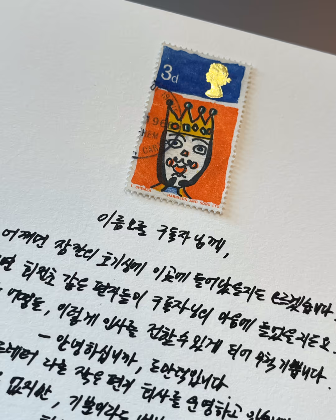 왕관을 쓴 얼굴이 그려진 영국 우표가 손글씨 편지 위에 놓여 있다.