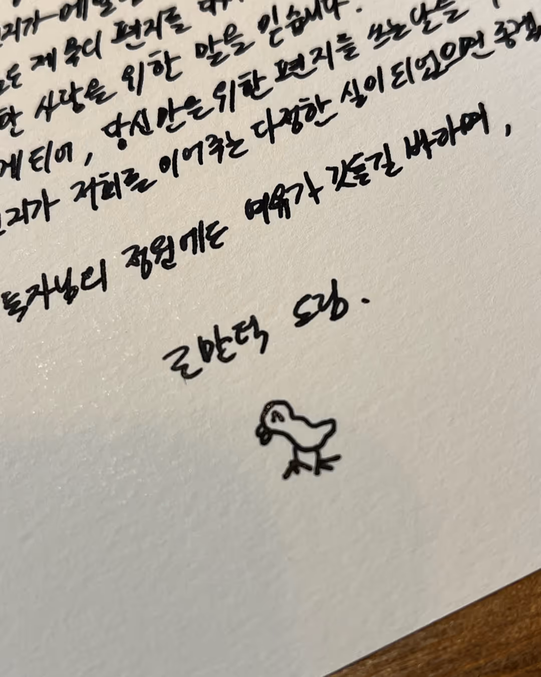 손글씨로 쓴 한국어 편지와 하단에 새 한 마리 그림이 그려져 있는 종이.