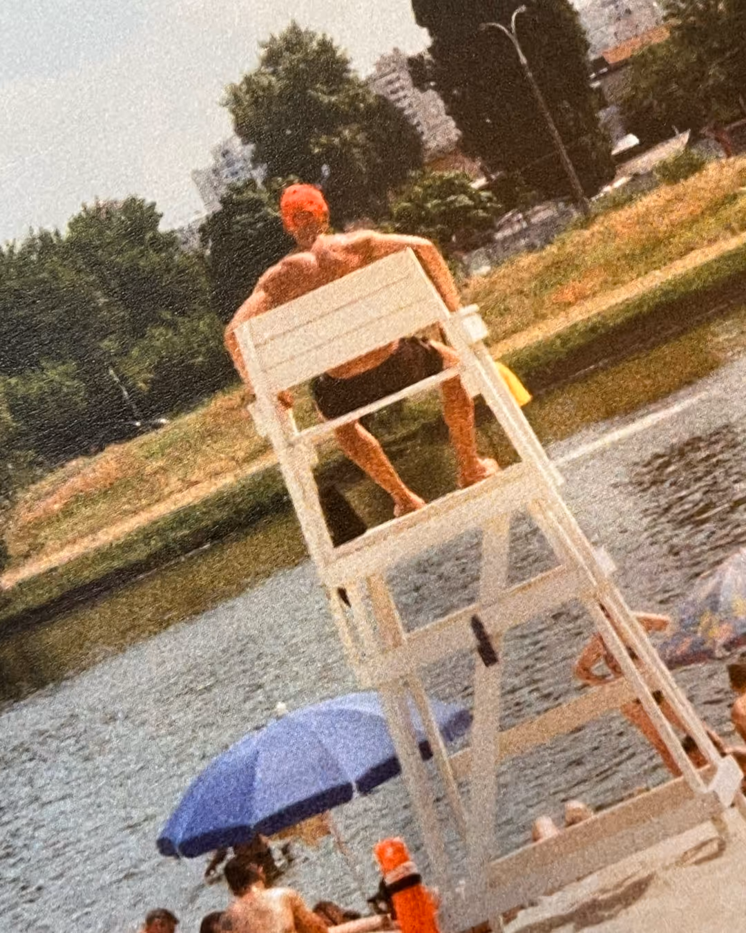 오렌지 수영모를 쓴 라이프가드가 하얀 관람대에서 물놀이하는 사람들을 지켜보고 있다.