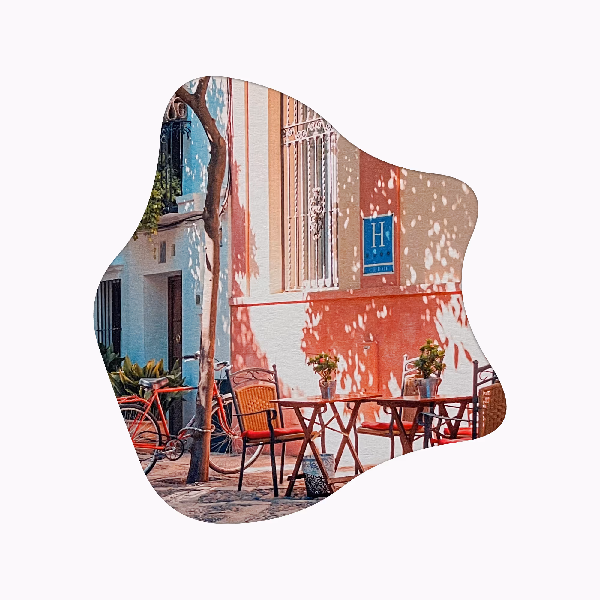 햇빛 아래 빨간 의자와 작은 나무 테이블들, 벽에 H 표시가 있는 건물이 있는 야외 카페 테라스.