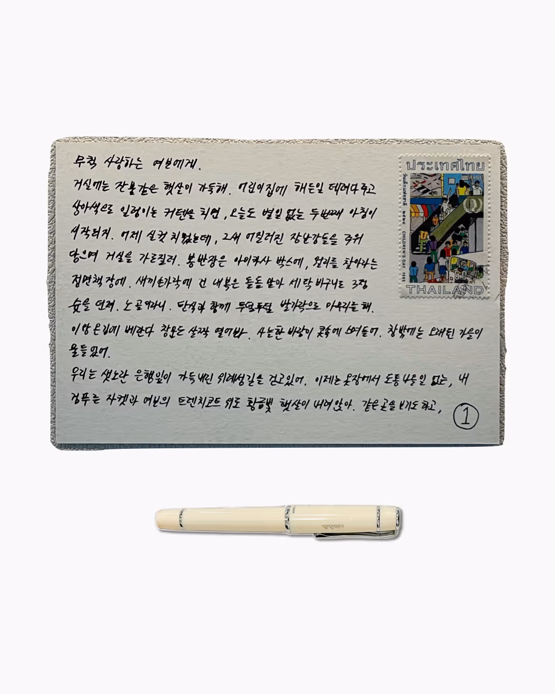 필체로 쓴 긴 편지와 태국 우편 소인이 찍힌 우표가 붙어 있고, 아래에 흰색 만년필이 놓여 있음.