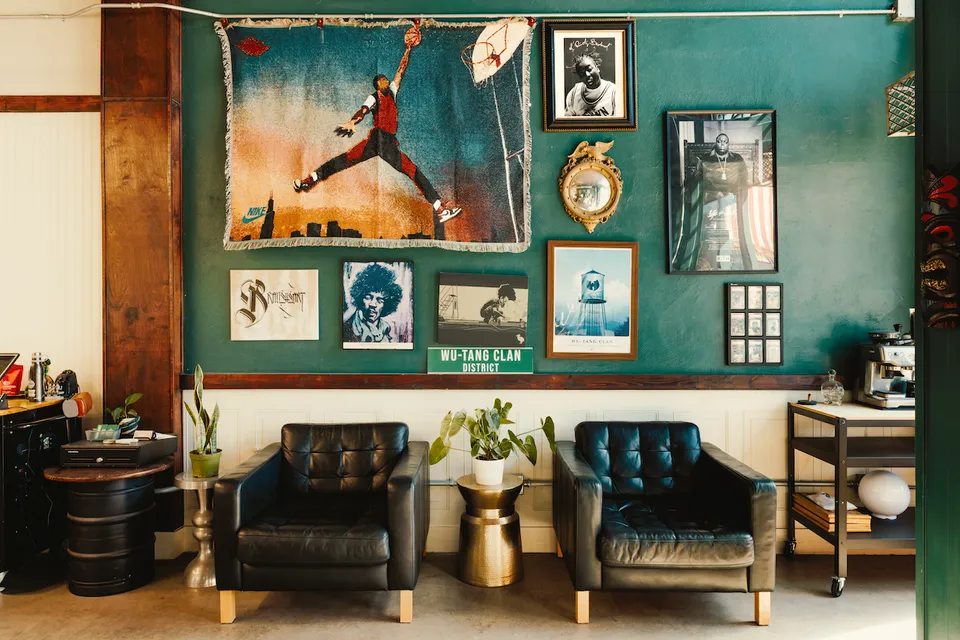 Waiting area at Braveheart Barbershop with two leather armchairs against a teal wall of framed art and prints