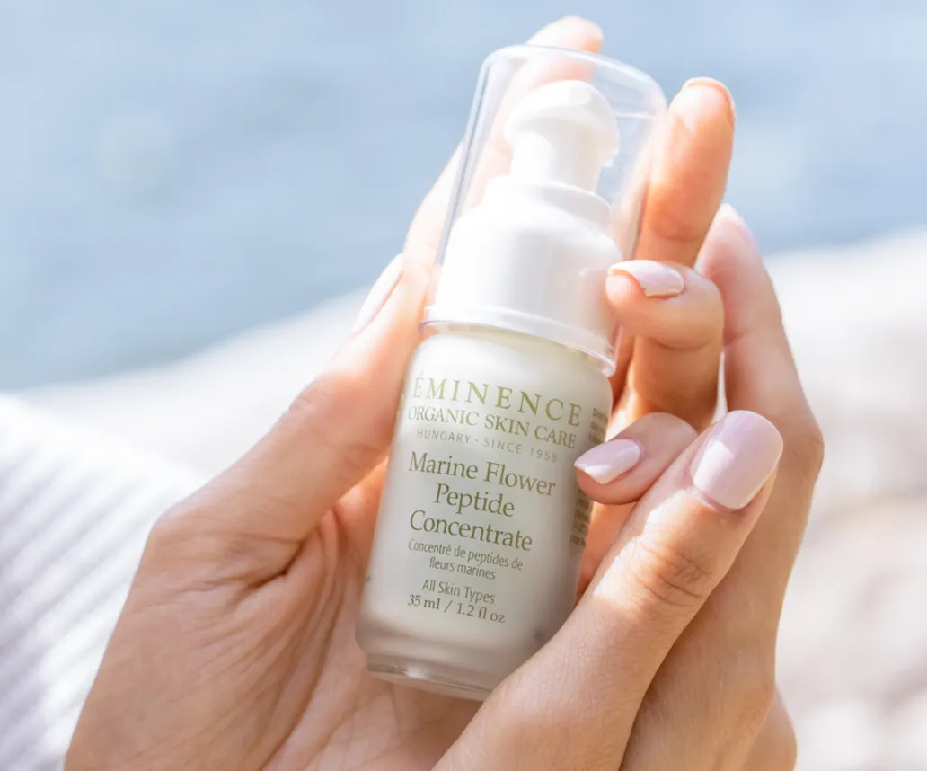 Hand holding a bottle of Éminence Organic Skin Care Marine Flower Peptide Concentrate serum.