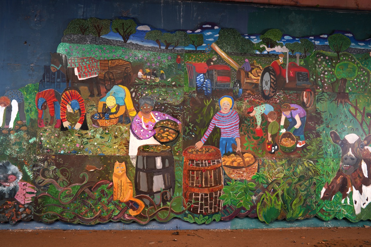 A painted section of the Alloway Tunnel mural showing people working the land and tending to an agriculture field.