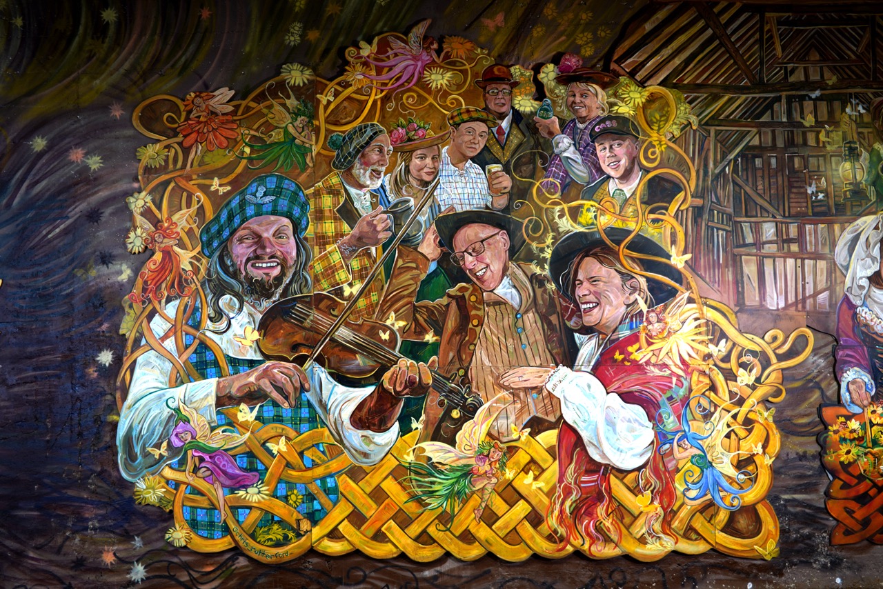 A painted section of the Alloway Tunnel mural showing trustees and Chris Rutterford dressed in traditional scottish clothing and celebrating. Chris is playing the violin.