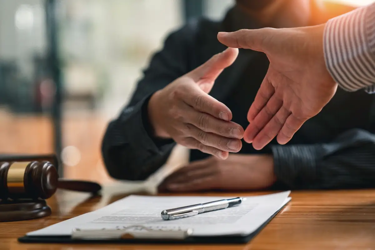 Two people are shaking hands over a desk with a wooden hammer and papers.
